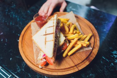 Peynirli klüp sandviç, turşulu kraker, domates ve füme et. Patates kızartmasıyla süslenmiş..