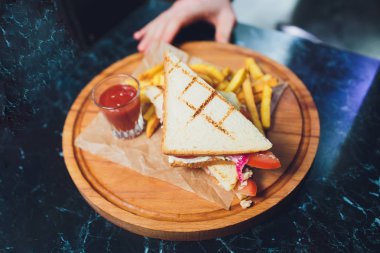 Peynirli klüp sandviç, turşulu kraker, domates ve füme et. Patates kızartmasıyla süslenmiş..