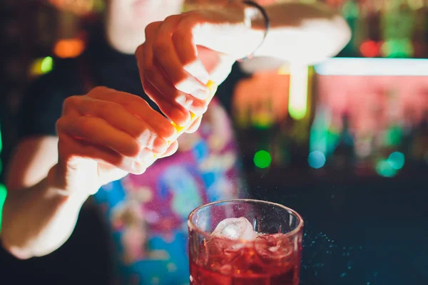 As mãos de Barman polvilhando o suco no copo de coquetel cheio de bebida alcoólica no fundo escuro . — Fotografia de Stock