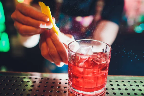 Бармен руки посыпать сок в коктейль стакан, наполненный алкогольным напитком на темном фоне . — стоковое фото