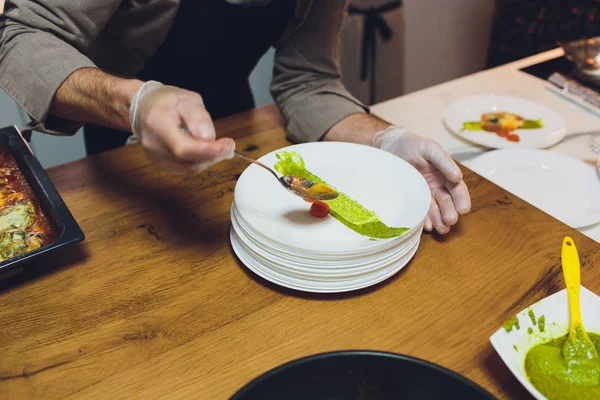 Un chef masculino decora un plato de ensalada en una cocina de restaurante en un delantal negro. primer plano de una mano con pinzas . — Foto de Stock