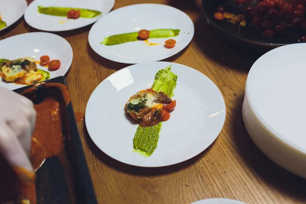 Un chef masculino decora un plato de ensalada en una cocina de restaurante en un delantal negro. primer plano de una mano con pinzas . — Foto de Stock