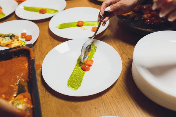 Un chef masculino decora un plato de ensalada en una cocina de restaurante en un delantal negro. primer plano de una mano con pinzas . — Foto de Stock