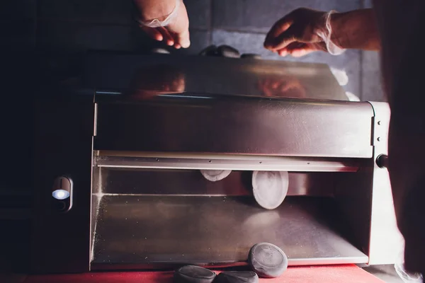 Chef-kok het maken van deeg gebak deegafwerkeenheid bakkerij Baker vormen shaping deeg gerold gebak metaalwerk tafel close-up handen proces van het voorbereiden van brood khinkali deegroller machine dunne pasta blad Top View — Stockfoto