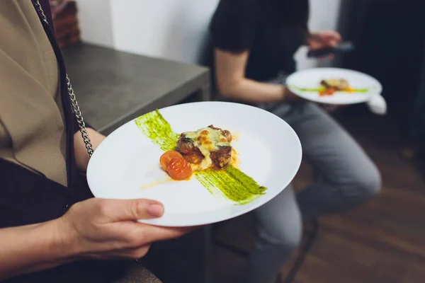 Un chef masculino decora un plato de ensalada en una cocina de restaurante en un delantal negro. primer plano de una mano con pinzas . — Foto de Stock
