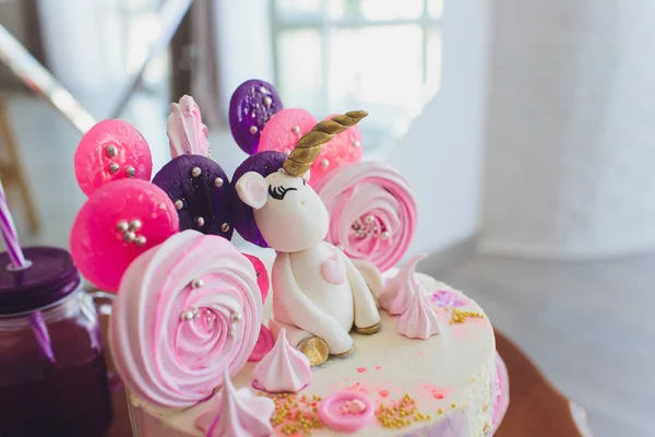 A beautiful bright cake decorated in the form of fantasy unicorn in the blue bookcase. The concept of a festive dessert for kids birthday.