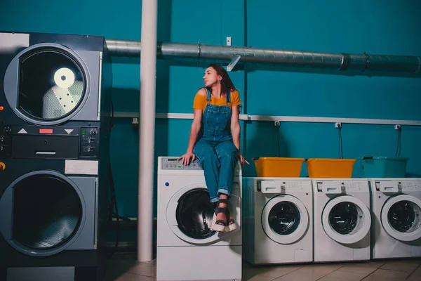 Wanita muda yang mencari pakaian di mesin cuci drum di binatu . — Stok Foto