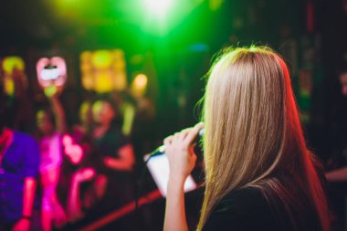 Bir mikrofon şarkı ve tatil parlayan arka plan üzerinde dans ile Güzellik modeli kız şarkıcı. Karaoke partisi şarkıcısı. Disko partisi. Kutlama.