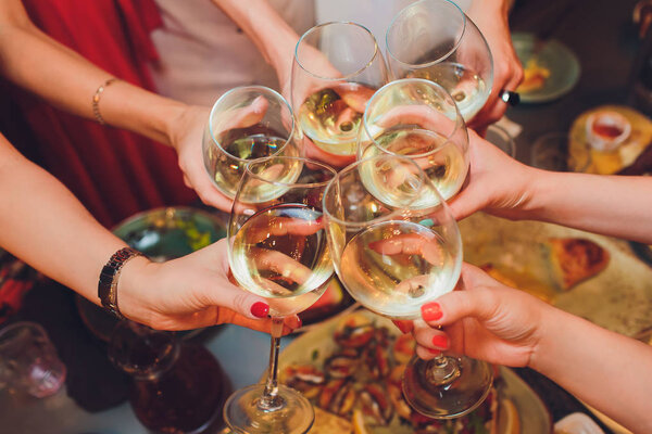 Human hands with glasses of red wine clinking them over served table.
