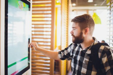 Bir adam fast-food restoranda elektronik menü ile dokunmatik ekran terminalinde yiyecek sipariş.