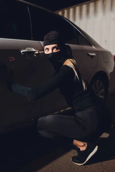 Masked robber woman car The thief is levering the lock at the door car robbery.