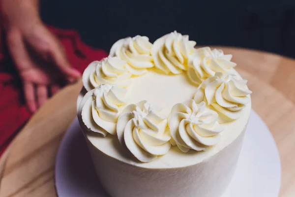 Confeiteiro decorado com bagas um bolo de biscoito com nata branca. Bolo fica em uma mesa de madeira. O conceito de pastelaria caseira, bolos de cozinha . — Fotografia de Stock