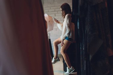 Mutlu genç kadın alışveriş çantaları ile giyim mağazasında oturan ve cep telefonu konuşuyor.