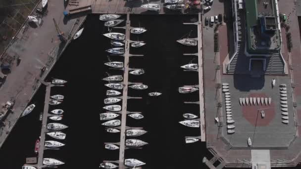 Widok z lotu ptaka przez Drone of Yacht Club i Marina. Widok na klub jachtowy. Białe łodzie w wodzie morskiej. Marina dok jachty i małe łodzie motorowe. Jacht i żaglówka są zacumowane na nabrzeżu. Parking. — Wideo stockowe