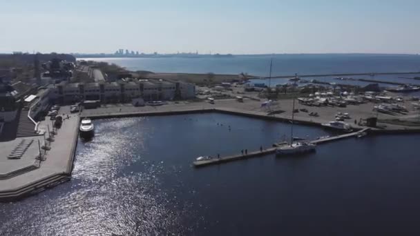 Widok z lotu ptaka przez Drone of Yacht Club i Marina. Widok na klub jachtowy. Białe łodzie w wodzie morskiej. Marina dok jachty i małe łodzie motorowe. Jacht i żaglówka są zacumowane na nabrzeżu. Parking. — Wideo stockowe