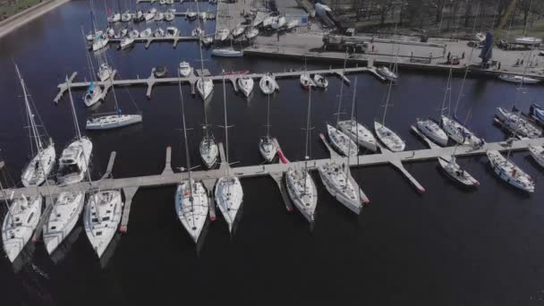 Widok z lotu ptaka przez Drone of Yacht Club i Marina. Widok na klub jachtowy. Białe łodzie w wodzie morskiej. Marina dok jachty i małe łodzie motorowe. Jacht i żaglówka są zacumowane na nabrzeżu. Parking. — Wideo stockowe