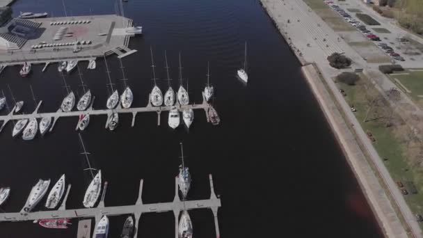 Widok z lotu ptaka przez Drone of Yacht Club i Marina. Widok na klub jachtowy. Białe łodzie w wodzie morskiej. Marina dok jachty i małe łodzie motorowe. Jacht i żaglówka są zacumowane na nabrzeżu. Parking. — Wideo stockowe