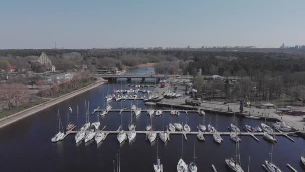 Widok z lotu ptaka przez Drone of Yacht Club i Marina. Widok na klub jachtowy. Białe łodzie w wodzie morskiej. Marina dok jachty i małe łodzie motorowe. Jacht i żaglówka są zacumowane na nabrzeżu. Parking. — Wideo stockowe