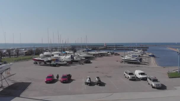 Widok z lotu ptaka przez Drone of Yacht Club i Marina. Widok na klub jachtowy. Białe łodzie w wodzie morskiej. Marina dok jachty i małe łodzie motorowe. Jacht i żaglówka są zacumowane na nabrzeżu. Parking. — Wideo stockowe