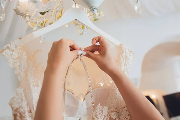 Vestido de noiva rosa rico pendura em um lustre em uma sala branca . — Fotografia de Stock