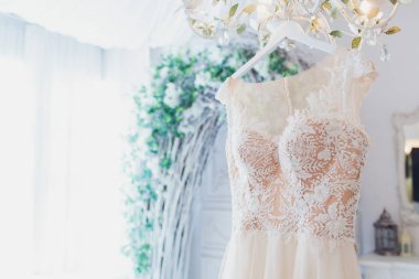 Zengin pembe gelinlik beyaz bir odada bir avize üzerinde asılı.