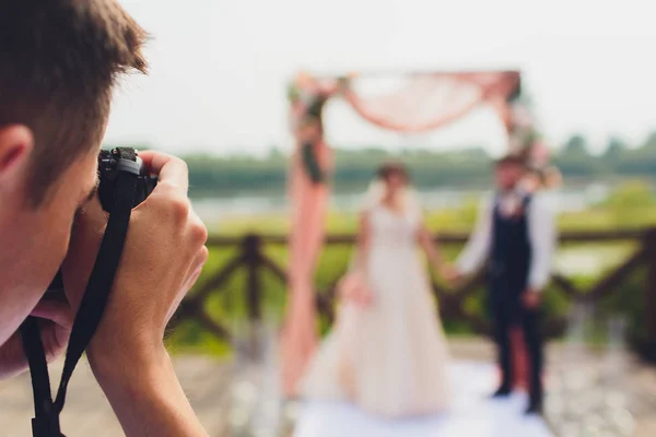 Wedding photographer takes pictures of bride and groom in city. wedding couple on photo shoot. photographer in action. — Stock Photo, Image