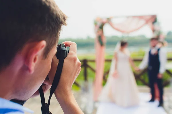 Wedding photographer takes pictures of bride and groom in city. wedding couple on photo shoot. photographer in action. — Stock Photo, Image