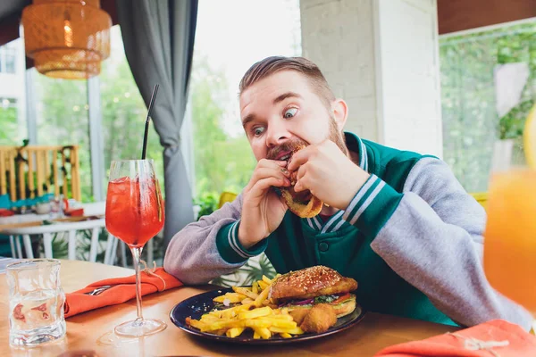 Picture of happy man eating vegan burger in vegan restaurant or cafe. Smiling man sitting at table.