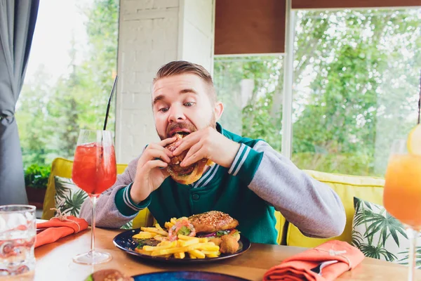 Picture of happy man eating vegan burger in vegan restaurant or cafe. Smiling man sitting at table.