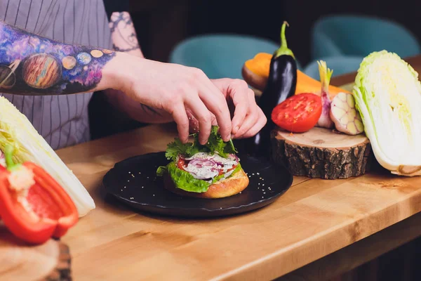 Chef haciendo saludables hamburguesas vegetarianas de salmón al aire libre en cocina abierta, odprta kuhna, evento del festival internacional de comida. Comida callejera lista para ser servida en un puesto de comida . — Foto de Stock