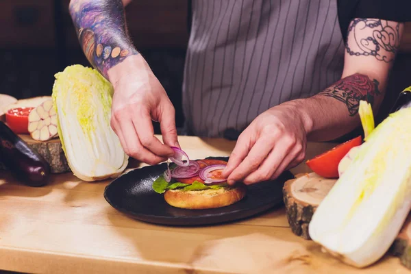 Chef haciendo saludables hamburguesas vegetarianas de salmón al aire libre en cocina abierta, odprta kuhna, evento del festival internacional de comida. Comida callejera lista para ser servida en un puesto de comida . — Foto de Stock