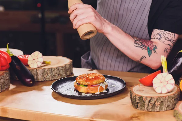 Chef haciendo saludables hamburguesas vegetarianas de salmón al aire libre en cocina abierta, odprta kuhna, evento del festival internacional de comida. Comida callejera lista para ser servida en un puesto de comida . — Foto de Stock