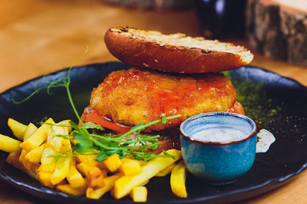 Vegetarian lentil burger in wholewheat bun with lettuce, tomato and cucumber accompanied by French fries Selective Focus, Focus on the front of the sandwich.