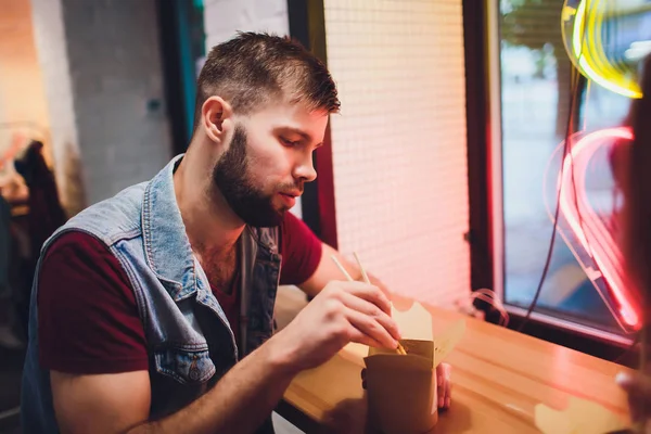 Concepto de comida callejera. Fideos japoneses chinos con pollo y verduras en utensilios de papel desechables. Espacio de copia, enfoque selectivo. sobre el fondo de una lámpara de neón en forma de corazón . — Foto de Stock