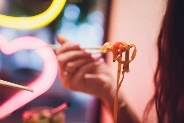 Concepto de comida callejera. Fideos japoneses chinos con pollo y verduras en utensilios de papel desechables. Espacio de copia, enfoque selectivo. sobre el fondo de una lámpara de neón en forma de corazón — Foto de Stock