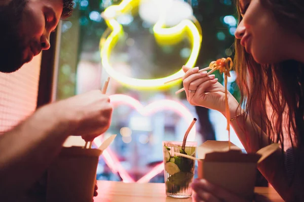 Концепция уличной еды. Китайская японская лапша с курицей и овощами в одноразовой бумажной посуде. Скопируйте пространство, избирательный фокус. на фоне неоновой лампы в форме сердца . — стоковое фото