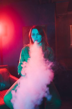kadın odada yatakta yatan bir e-sigara içiyor. Sigara içenler kavramı Vaping.