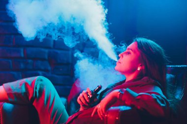 kadın odada yatakta yatan bir e-sigara içiyor. Sigara içenler kavramı Vaping.