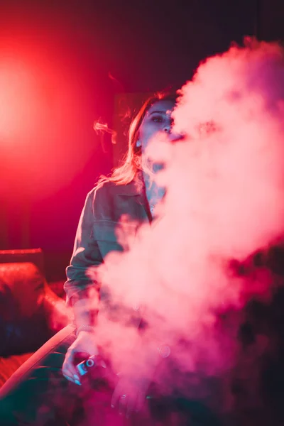 woman smokes a e-cigarette lying on the bed in the room. Smokers concept Vaping.