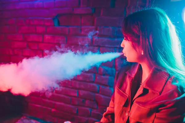 woman smokes a e-cigarette lying on the bed in the room. Smokers concept Vaping.