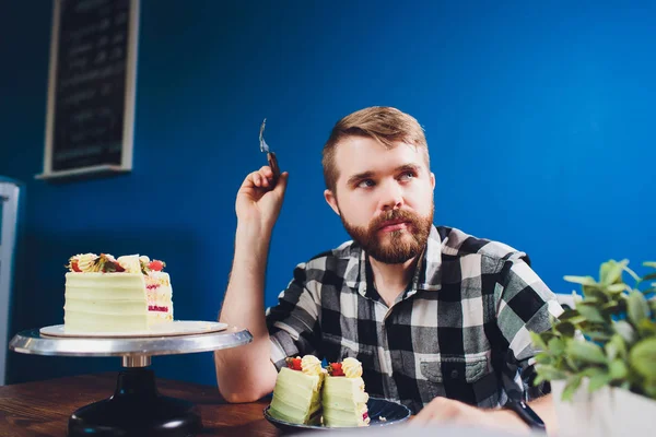 İnsanlar, eğlence, gıda kavramı - beyaz gömlek yakışıklı gülümseyen adam masada kahvaltı yeme oturuyor. Sabah kahvaltısı - sakallı adam lezzetli pasta yeme, masada fincan kapuçino veya kahve veya çay sahip.