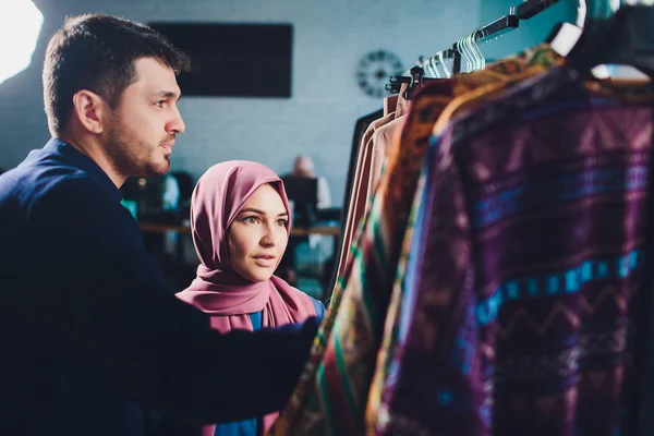Lächelndes junges muslimisches Paar beim Einkaufen und beim Anblick von Teppichen in einem Textilgeschäft. — Stockfoto