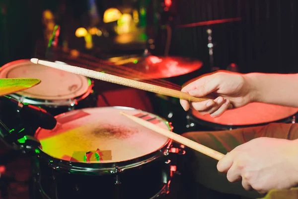 De man speelt de drums, het spel is op de trommel werken met stokken close-up. Op de achtergrond van de gekleurde lampen met spatten van water. Muzikaal concept met een trommel werken. — Stockfoto