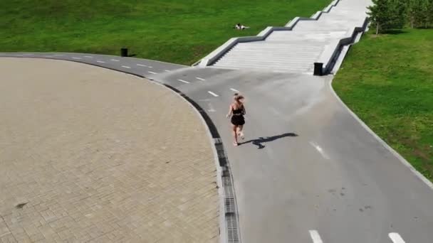 Vue de dessus de la jeune femme athlétique attrayante vitesse de course sur l'asphalte de la ville et l'entraînement dans la matinée par une journée d'été ensoleillée. Une coureuse s'entraîne en plein air. concept sportif . — Video