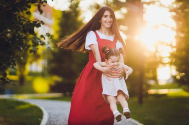 onlar güneşli bir günde parkta yürürken kollarında onu küçük kızı tutarak genç anne.