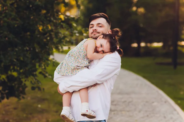 Fatherhood, family and leisure concept - father holding little daughter in his arms in park. — Stock Photo, Image