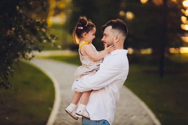 Fatherhood, family and leisure concept - father holding little daughter in his arms in park. — Stock Photo, Image