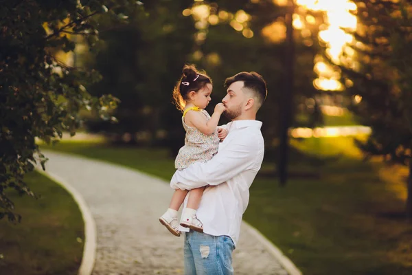 Fatherhood, family and leisure concept - father holding little daughter in his arms in park. — Stock Photo, Image