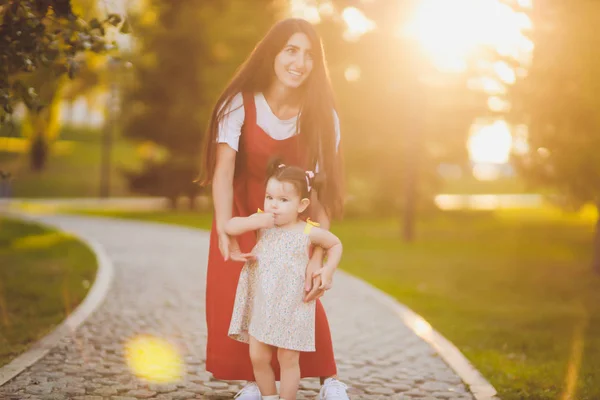 Jonge moeder houdt haar peuter dochter in haar armen als ze lopen door het Park op een zonnige dag. — Stockfoto