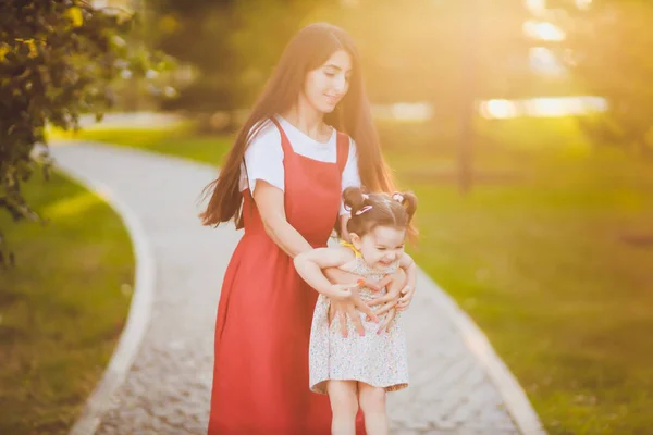 Jonge moeder houdt haar peuter dochter in haar armen als ze lopen door het Park op een zonnige dag. — Stockfoto